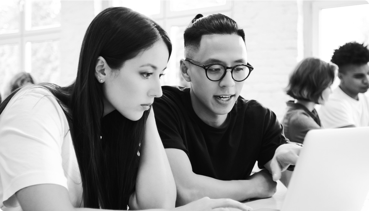 Two people sitting in front of a laptop in a classroom