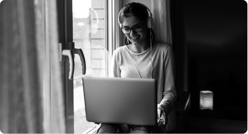 A person works on a laptop beside. a window.