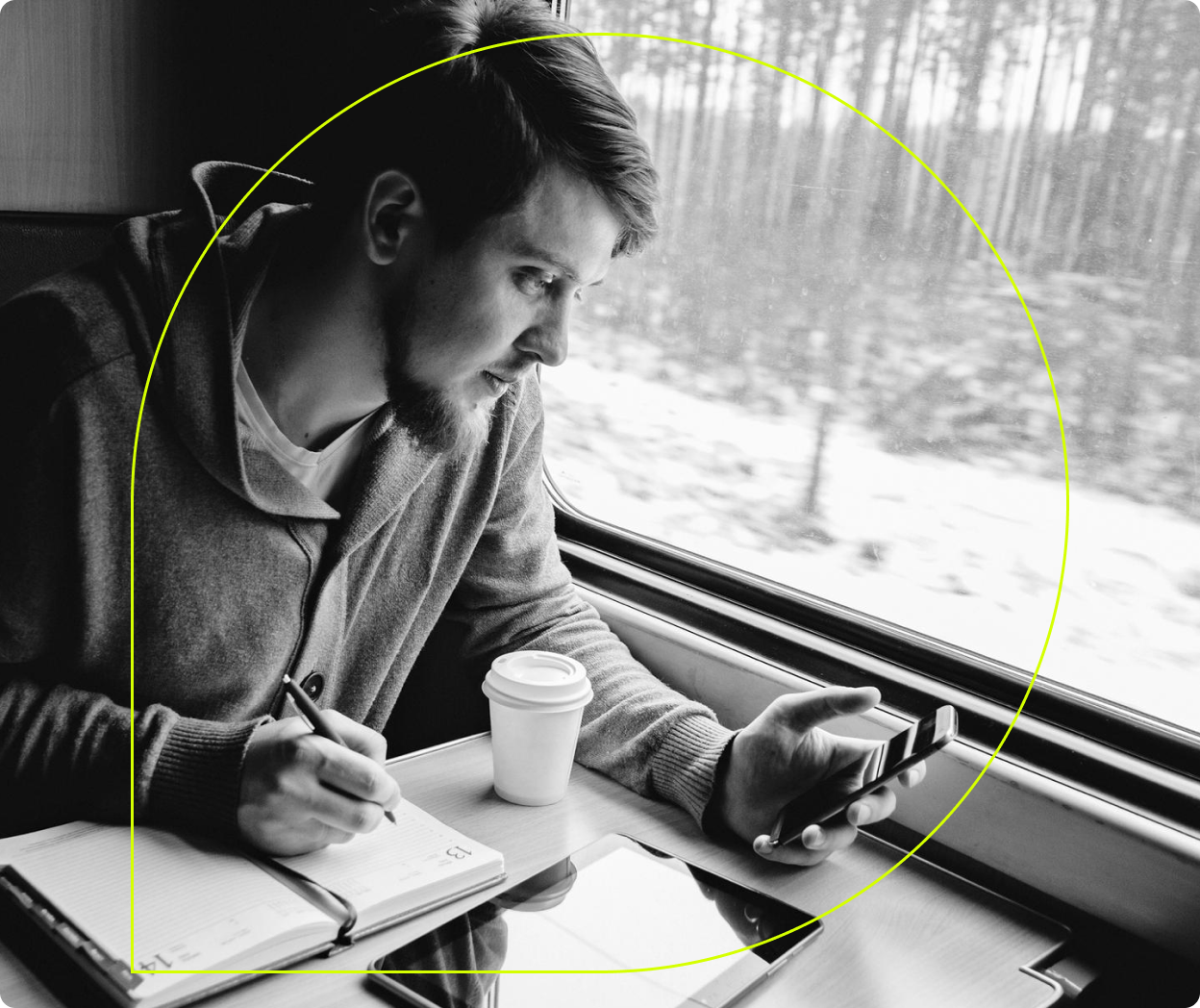 A person writes in a notebook on a train with an iPad on the table in front of them. 